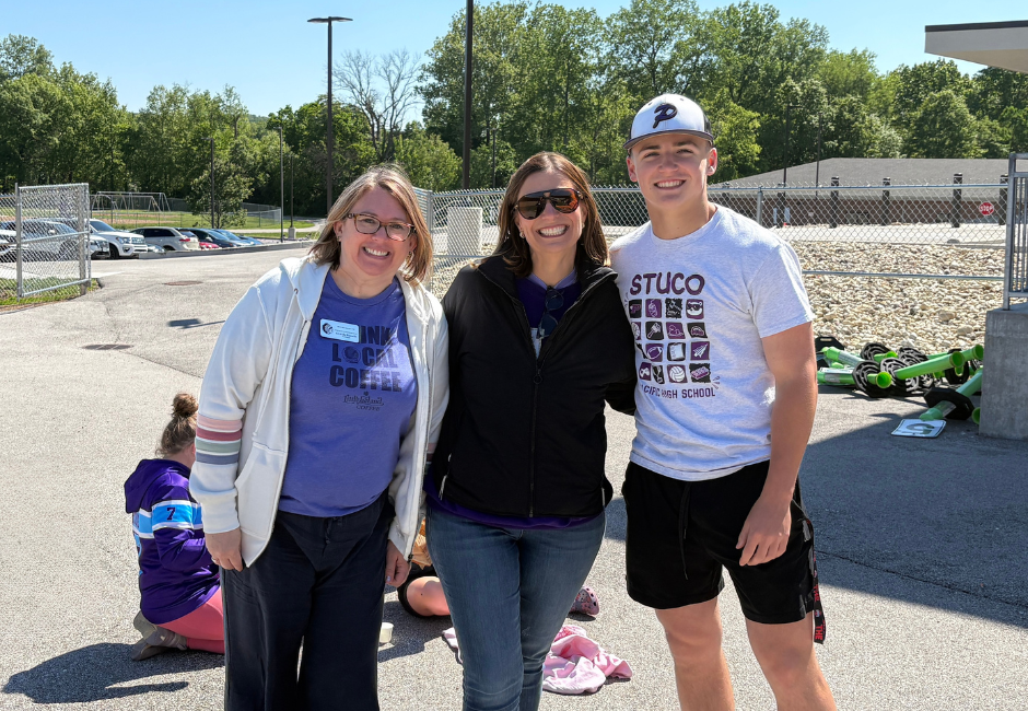 Two staff members pose with a student outside.