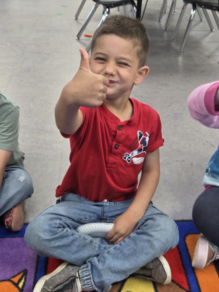 Young student wearing a red shirt holding a thumbs up at the camera while smiling.