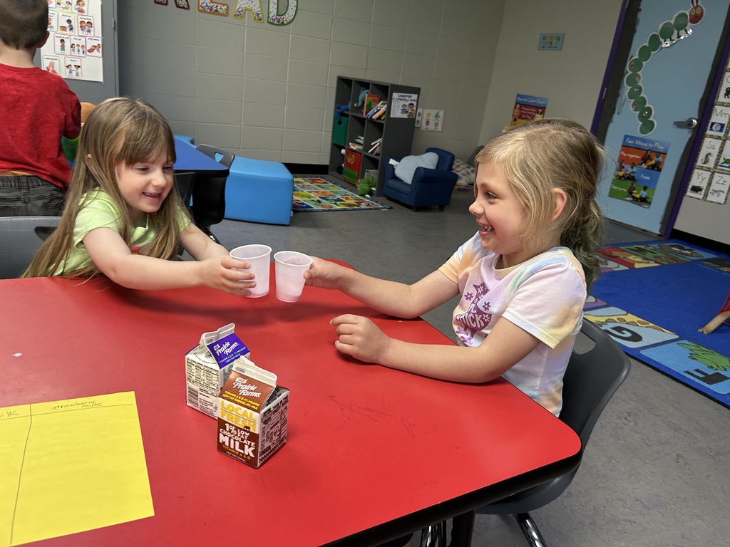 Two young students cheers two plastic cups at a red school table.