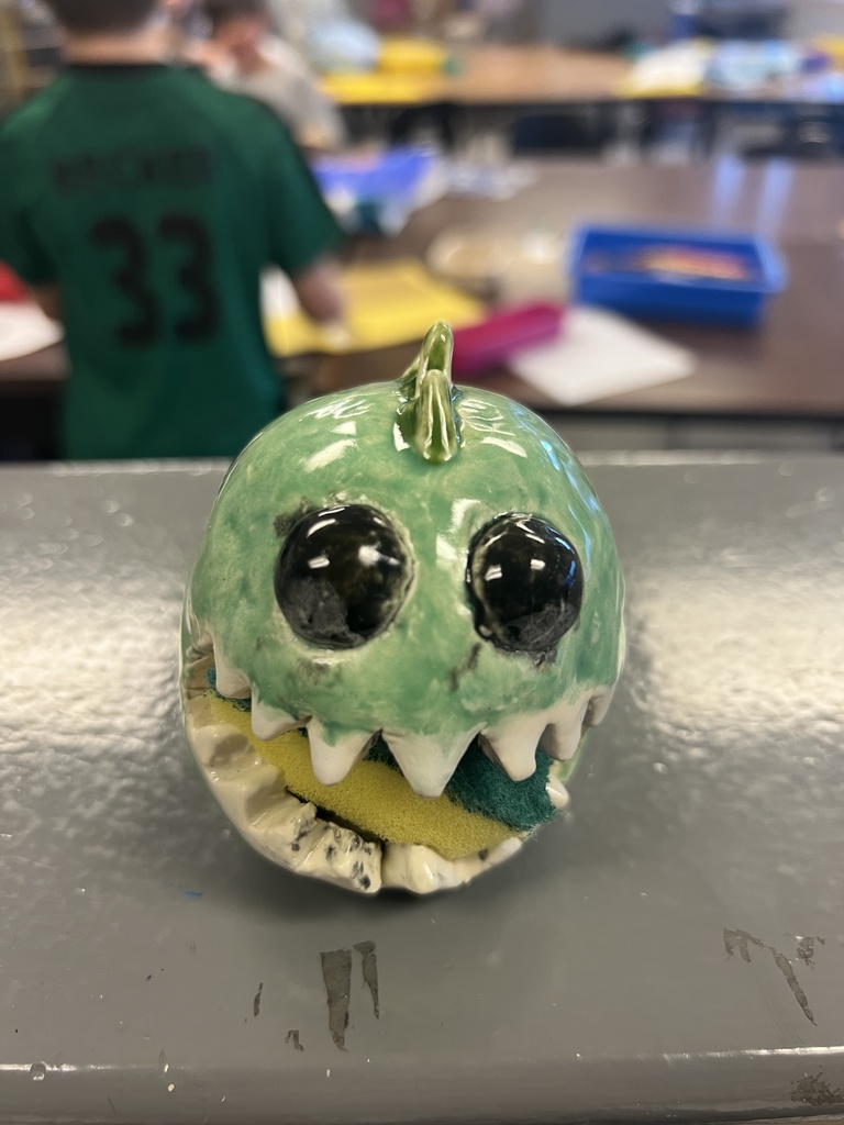 Small green ceramic shark sponge holder with black eyes, white teeth, and a sponge inside its mouth on a classroom table.