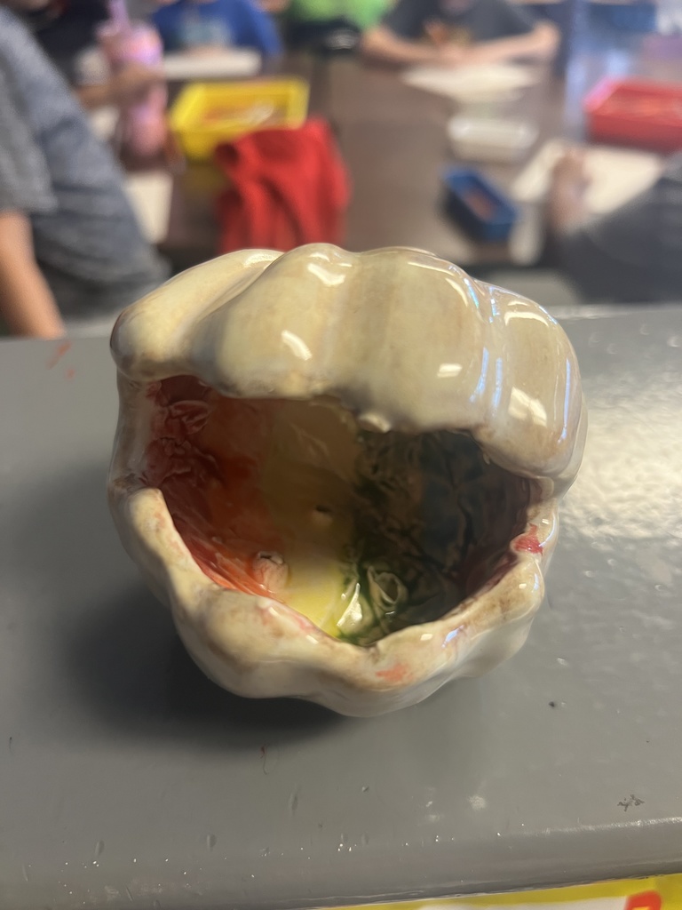 Glossy white ceramic sponge holder with a wide open mouth and colorful glaze details inside, photographed in a classroom.