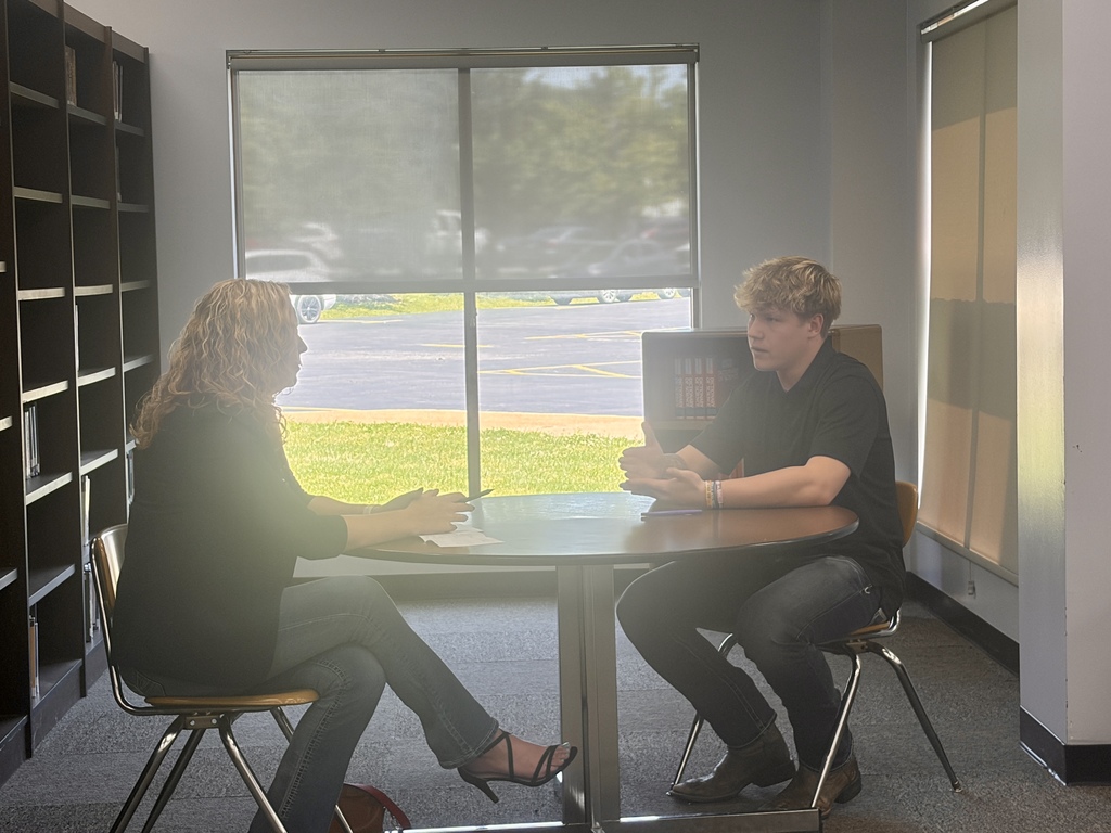 A student is talking with a staff member inside a school classroom.