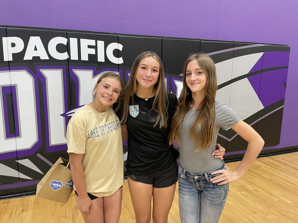Three student pose for a photo in a purple school gym.