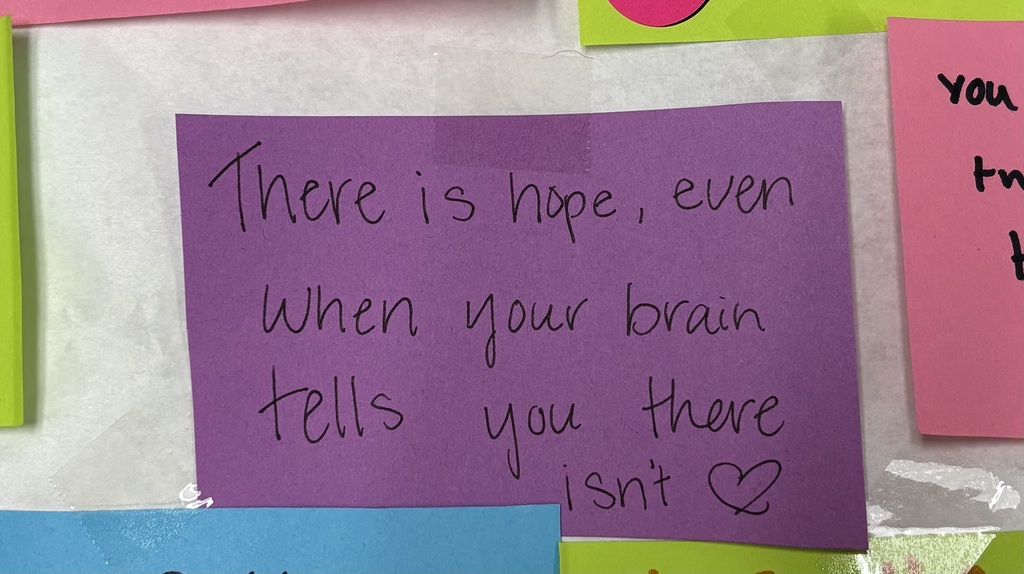 Purple sticky note reads, “There is hope, even when your brain tells you there isn’t,” on a mental health display.