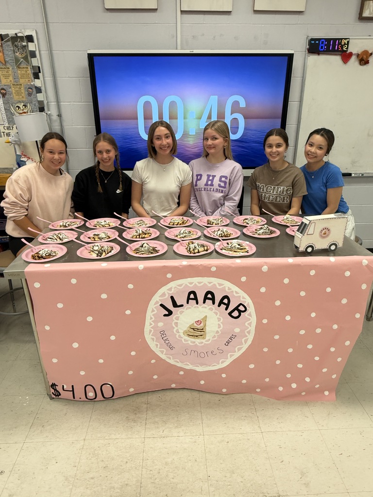 Six students sit behind plates of s’mores crepes at a pink-themed classroom food booth.