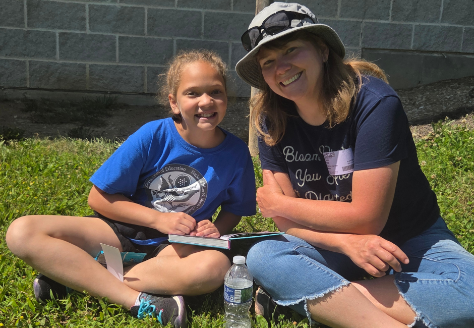 A student and a staff member reading outside smiling for a photo.