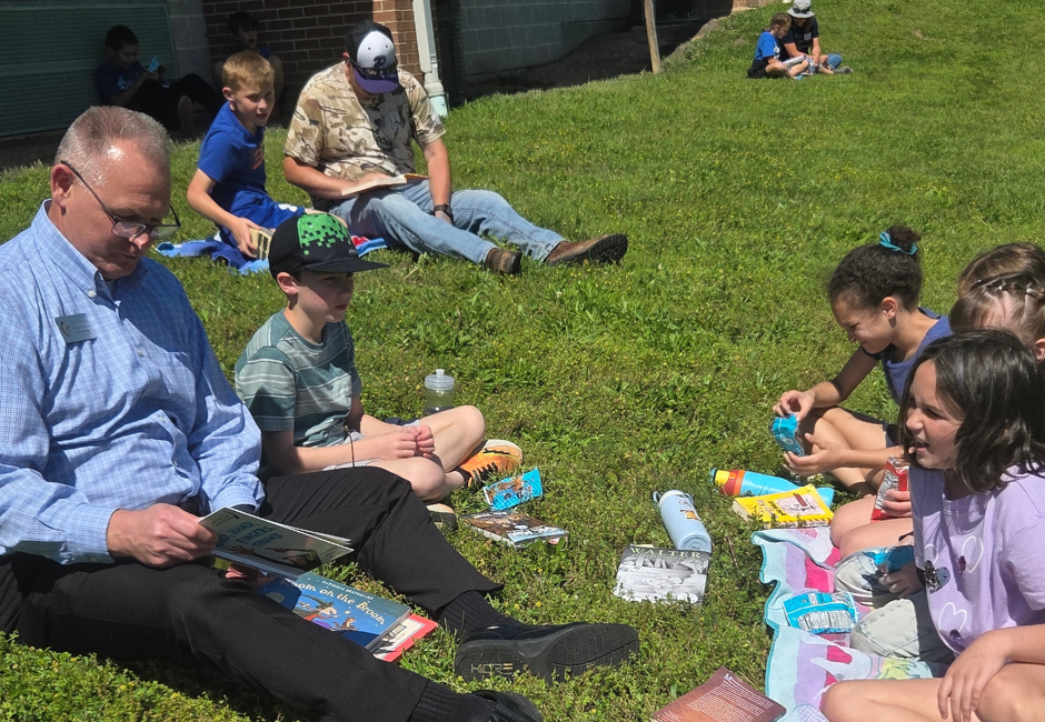Students with their families reading outside in the grass.