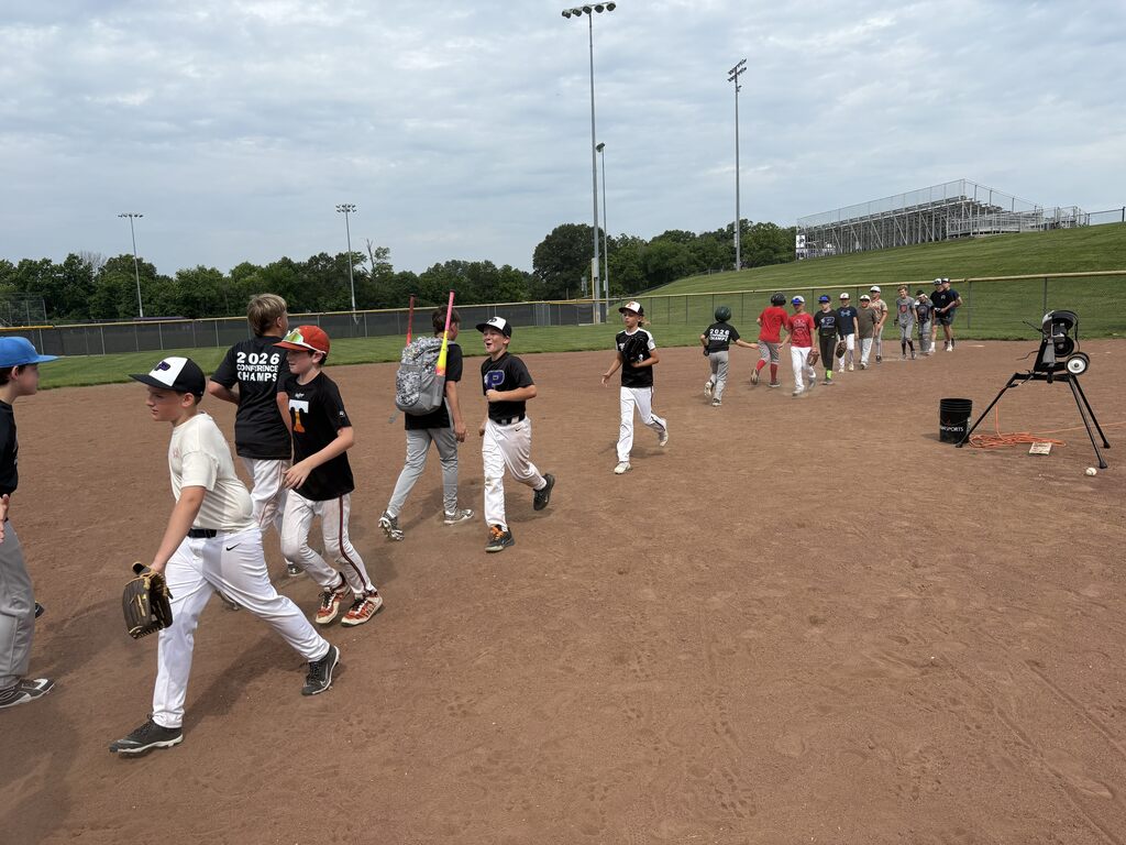 Youth baseball players exchange high fives and handshakes on the infield after a drill during a summer camp session.