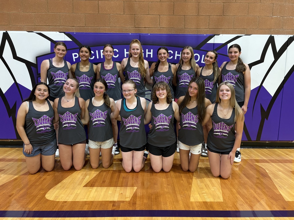 Teen basketball players wearing “Queens of the Court” camp shirts pose for a group photo in the Pacific High School gym.