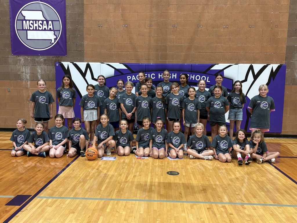 Youth girls basketball camp participants pose together in matching camp T-shirts on the Pacific High School gym floor.