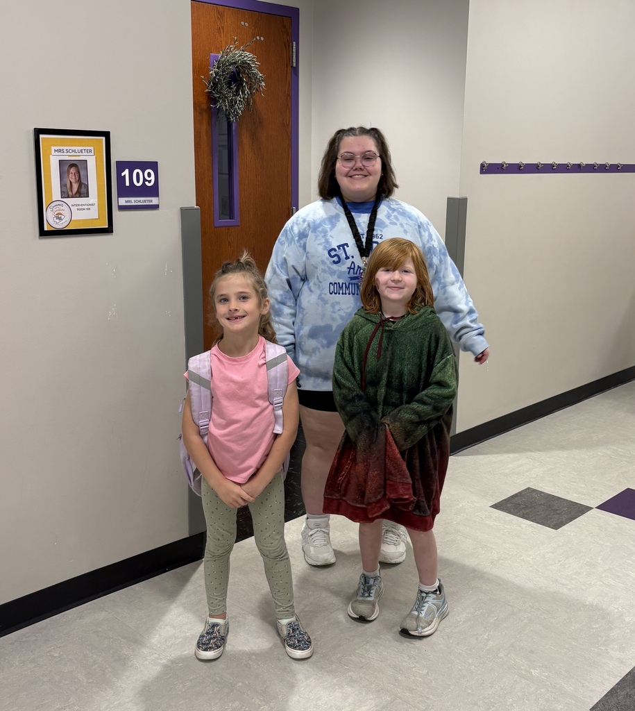 Two students post for a photo with a staff member in a school hallway.