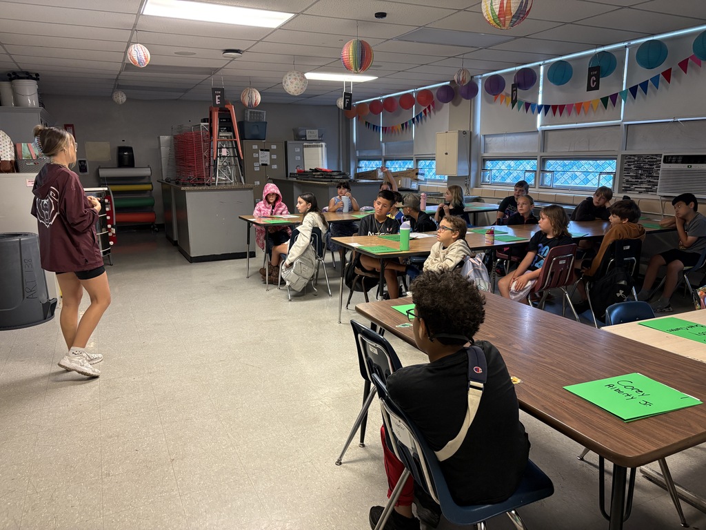 A staff member speaking to a group of students in a school classroom.
