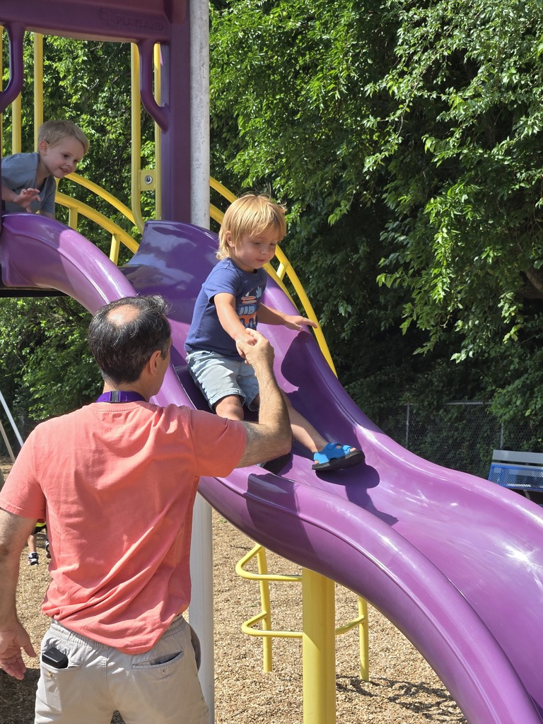 Staff member helping a student down a purple slide.