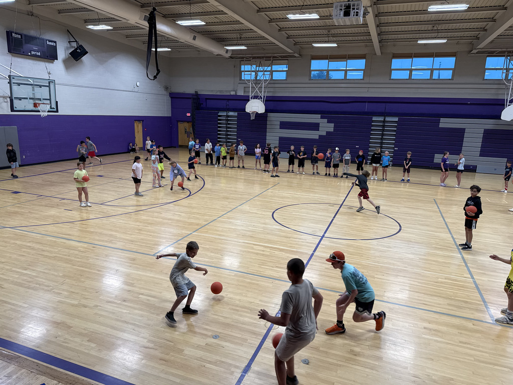 A large group of students playing dodgeball in a school gym.