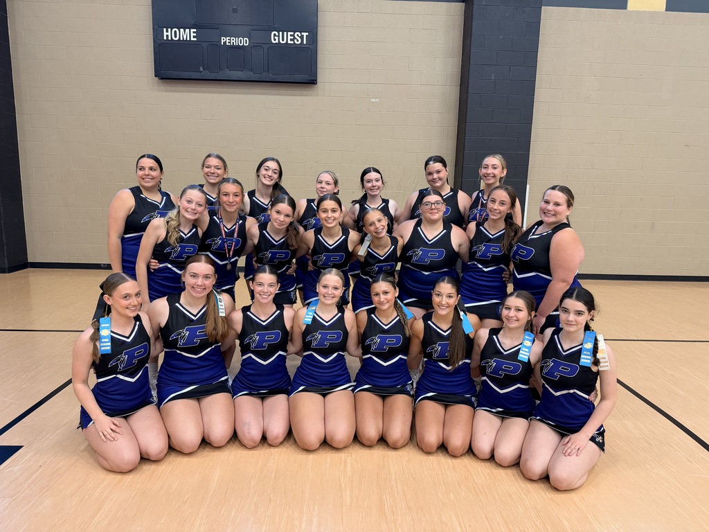 Pacific High School cheerleaders pose in a gym after a competition, wearing blue-and-black uniforms and displaying medals and award ribbons.