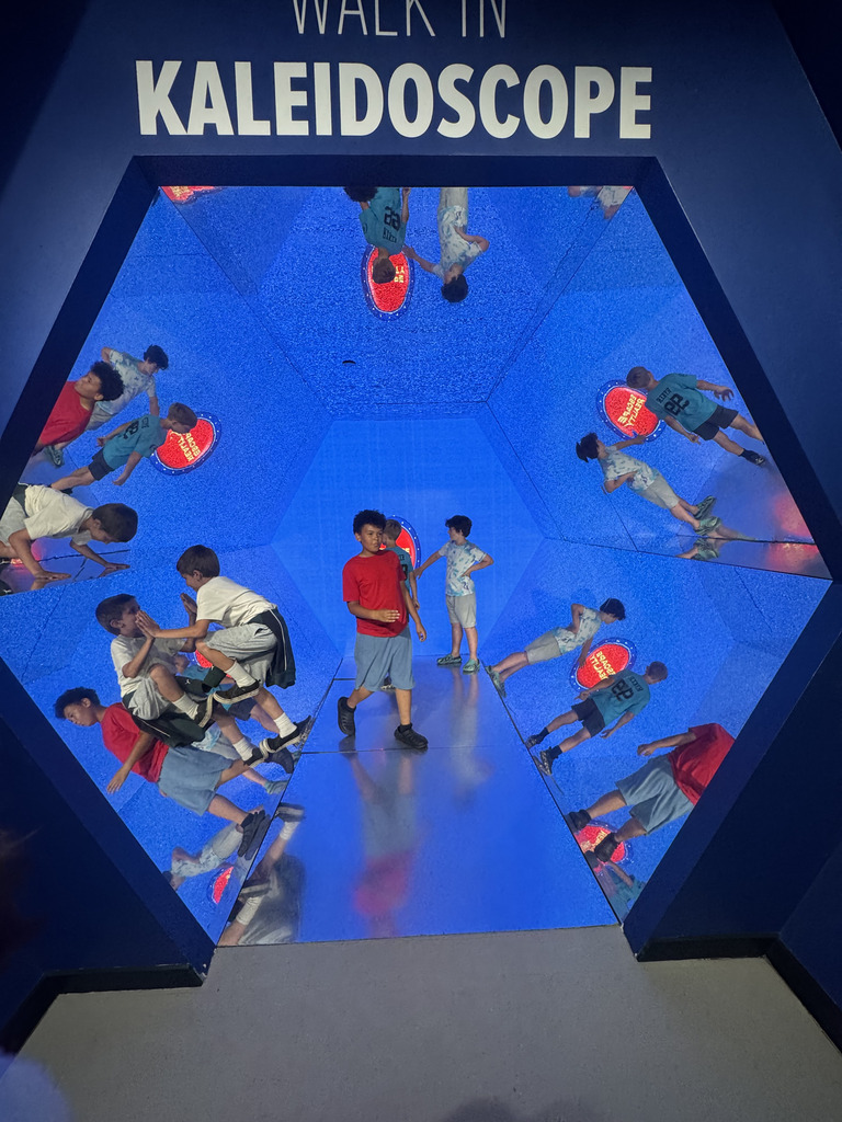 Students explore a walk-in kaleidoscope exhibit, surrounded by colorful mirrored reflections in every direction.