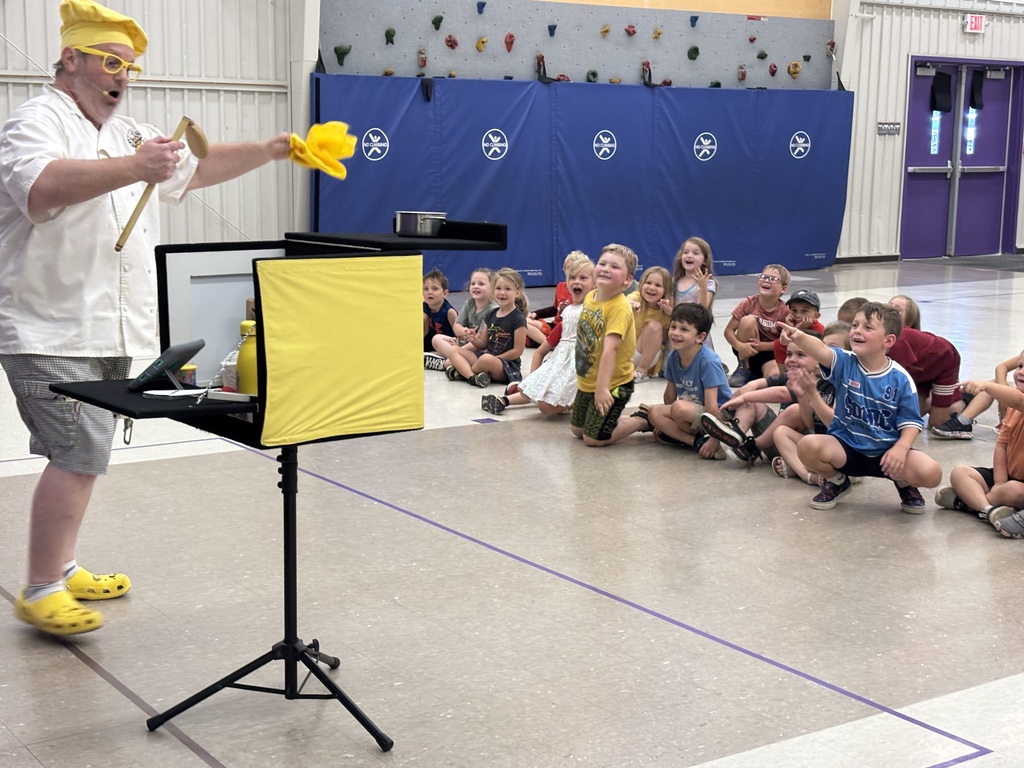 Students laugh and point as a chef-themed performer leads an interactive show in the gym.