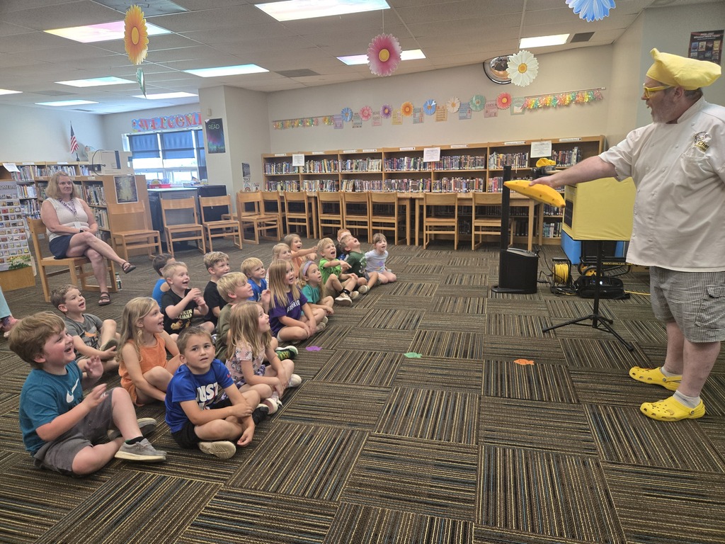 Students sit attentively in the library as a performer dressed as a chef entertains them with a lively presentation.