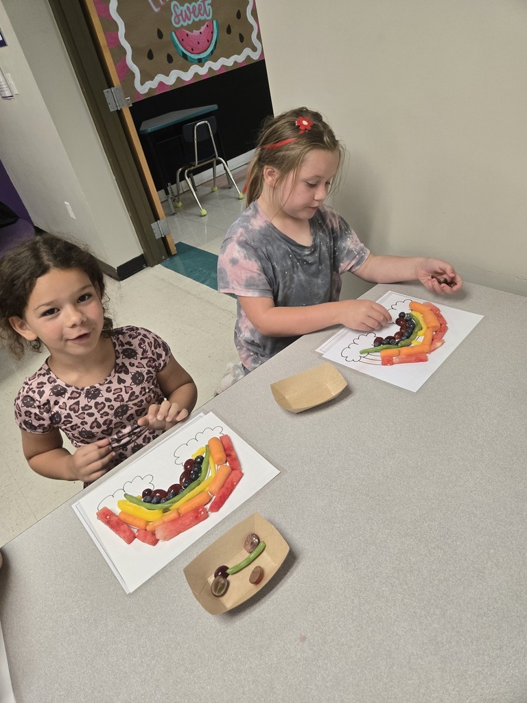 Two students create colorful rainbow designs with fruits and vegetables during a healthy eating activity.