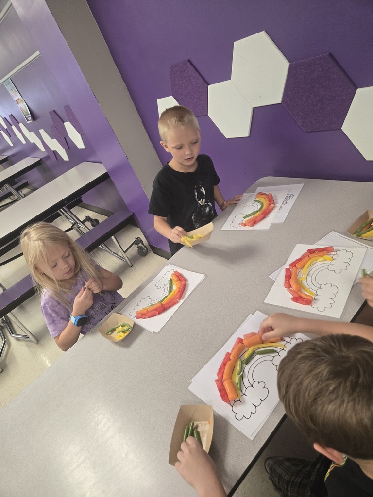 Students arrange fruits and vegetables into rainbow patterns on worksheets during a classroom nutrition lesson.