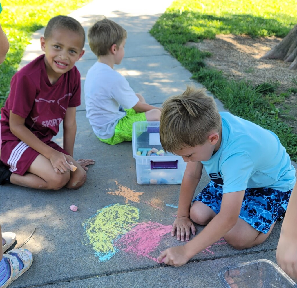 Students use colorful sidewalk chalk to create drawings during outdoor play time.