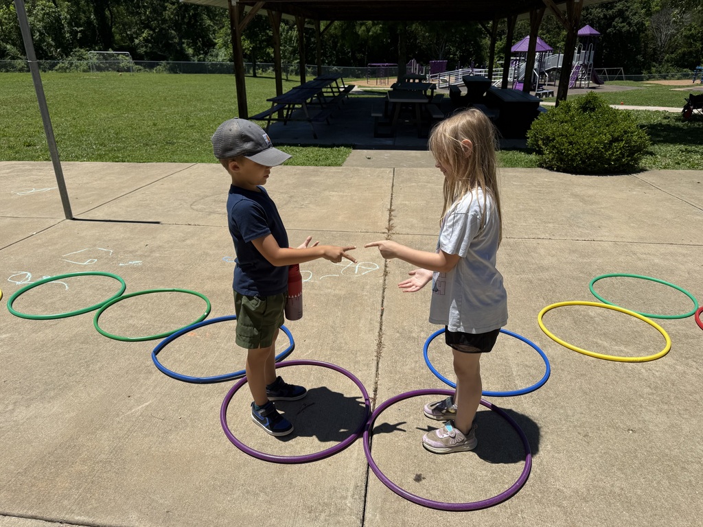 Two students play rock-paper-scissors while standing in hula hoops during an outdoor activity.