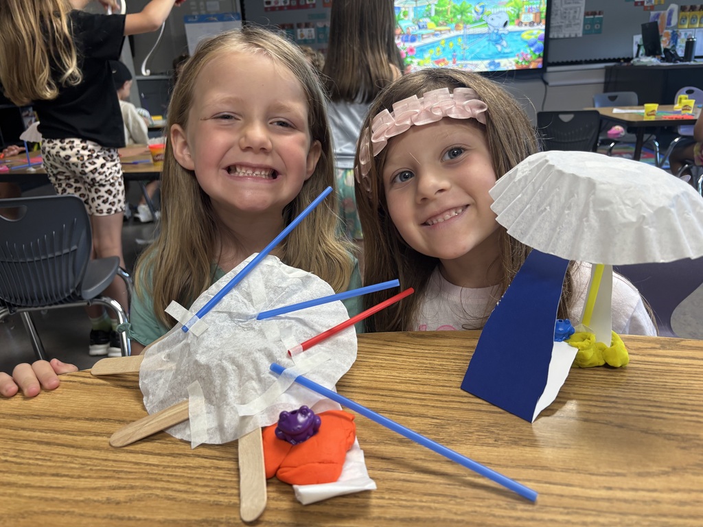 Two young students smiling in front of their art project.