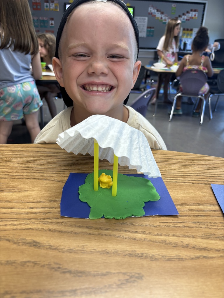 Young student smiling in front of their art project.