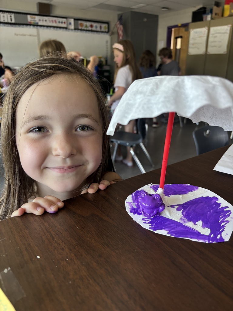 Young student smiling in front of their art project.