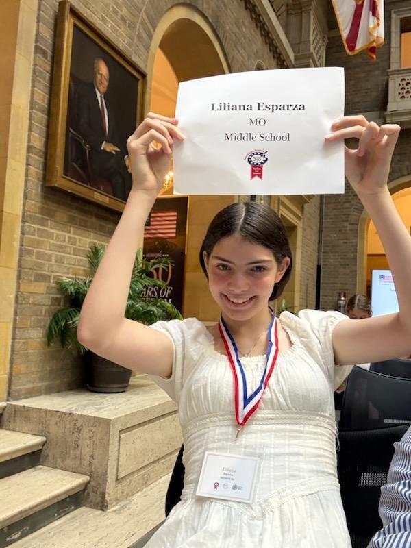 Student wearing a medal holds a sign recognizing her as a Missouri middle school winner in the American Heroes Student Art Contest.