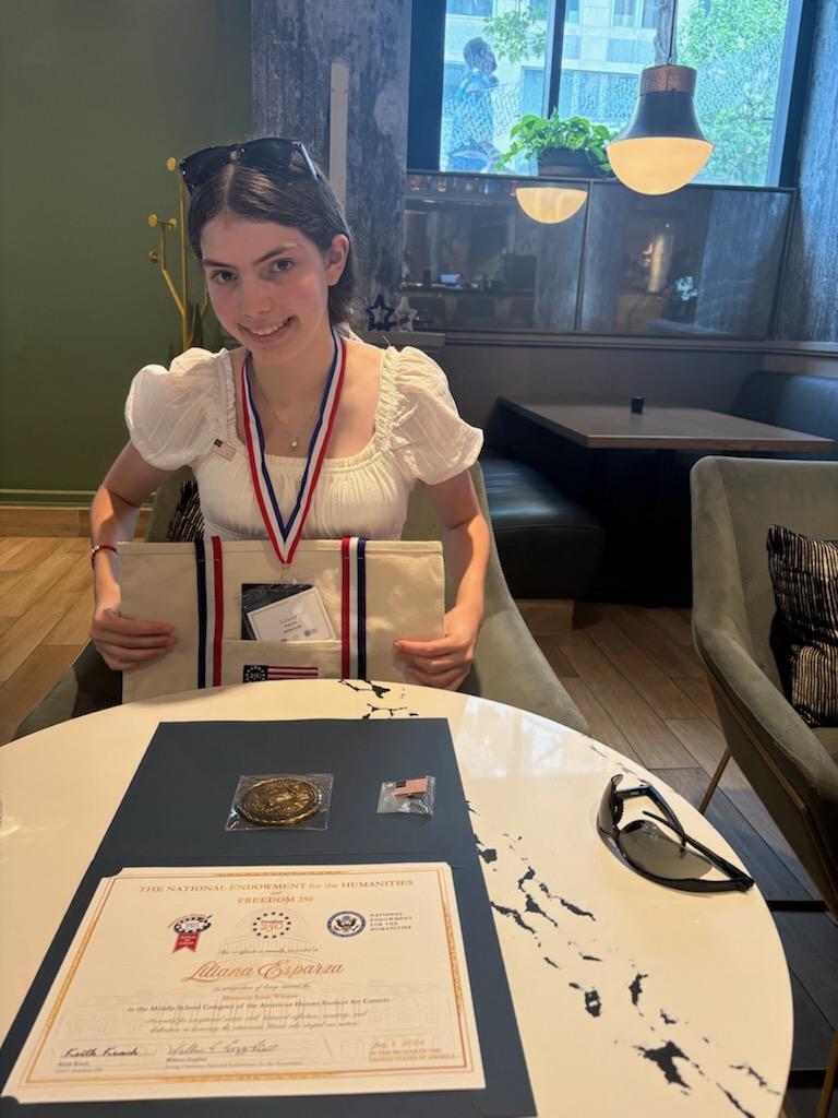 Student proudly displays a medal, certificate, and award from the American Heroes Student Art Contest.