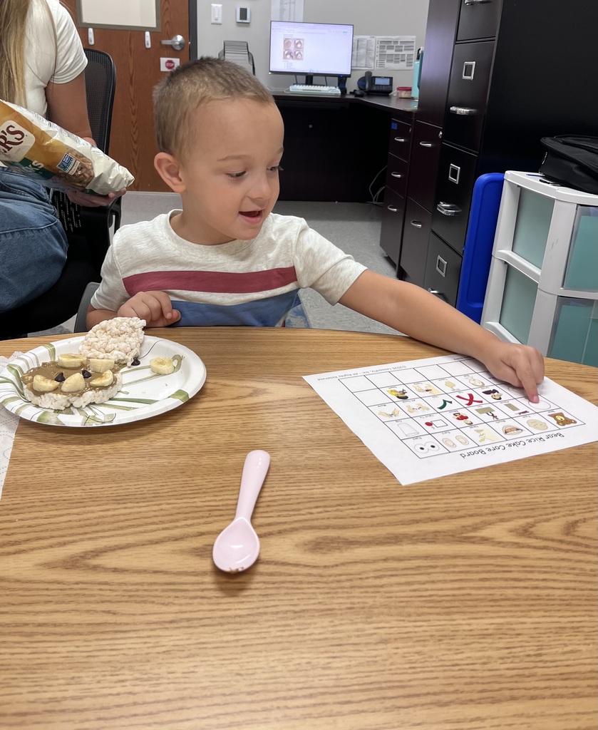 Young children participate in a snack-themed learning activity, matching foods on picture boards while enjoying healthy snacks around a classroom table.