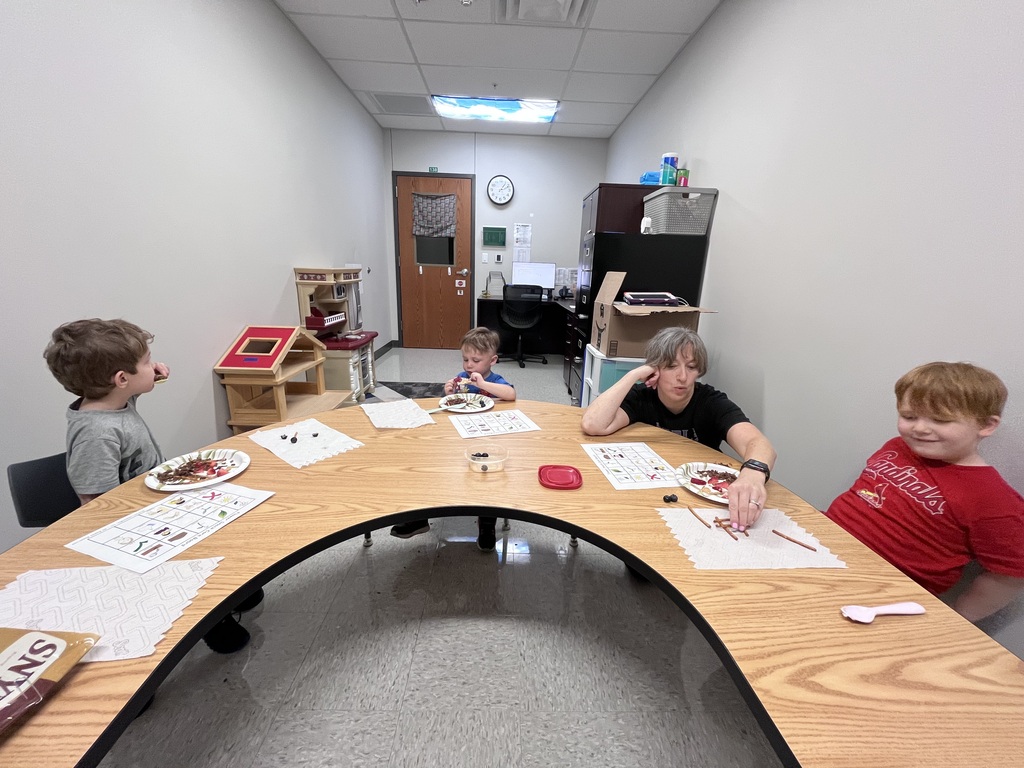 Young children participate in a snack-themed learning activity, matching foods on picture boards while enjoying healthy snacks around a classroom table.