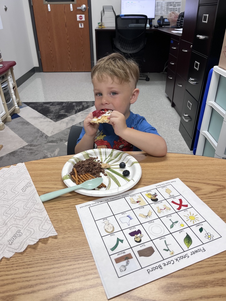 Young children participate in a snack-themed learning activity, matching foods on picture boards while enjoying healthy snacks around a classroom table.