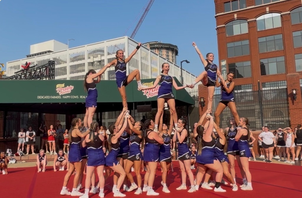 A group of cheerleaders in formation on a red carpet outdoors.