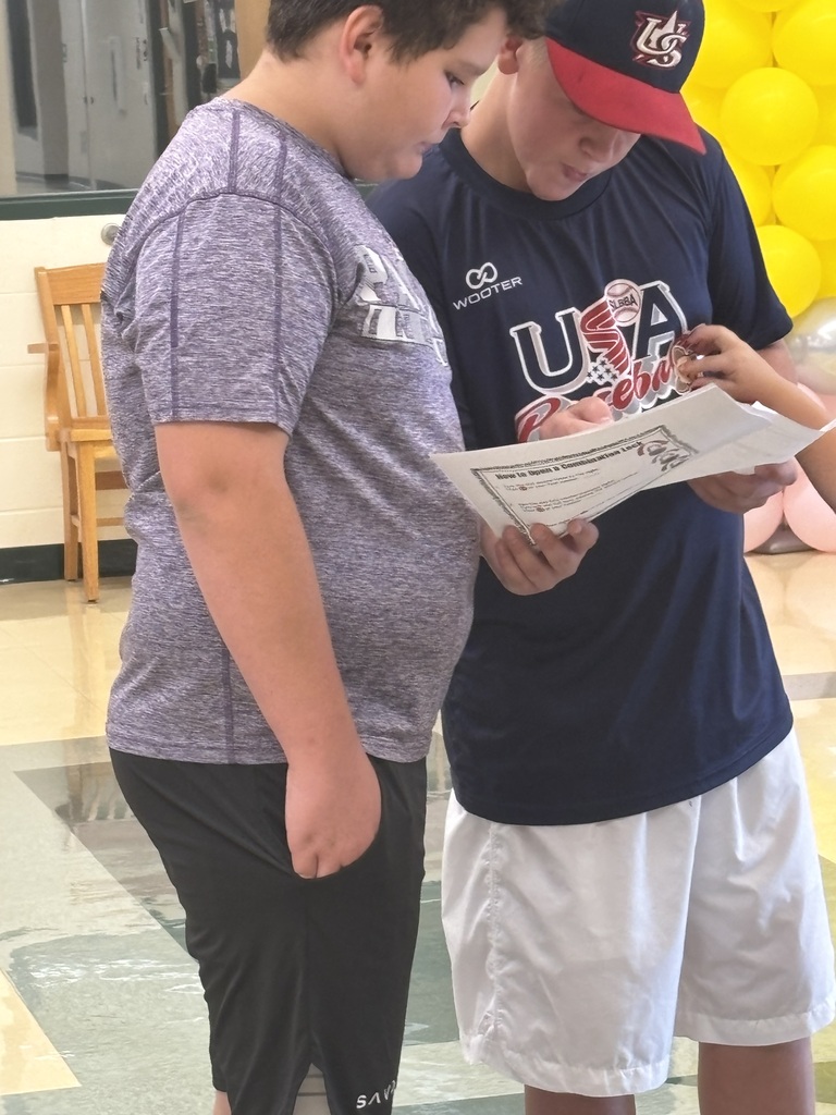 Two boys stand together reading a printed activity sheet during a school event.