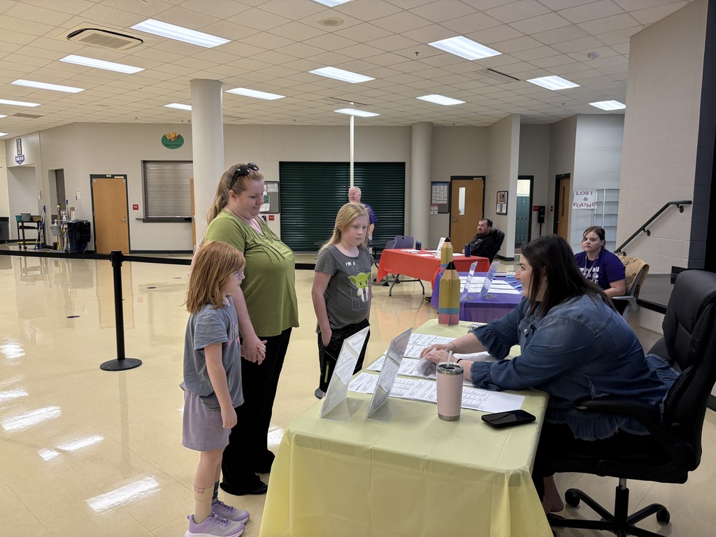A woman and two children speak with a staff member at an information table during a school event.