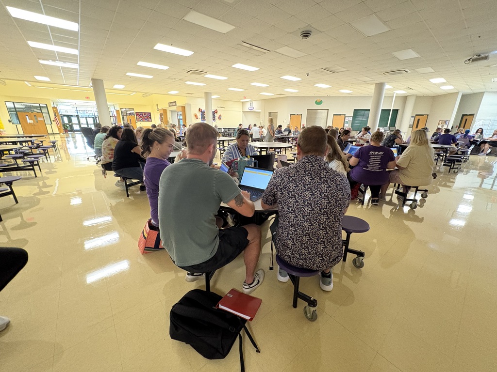 A speaker presenting to a room full of staff in a school cafeteria.