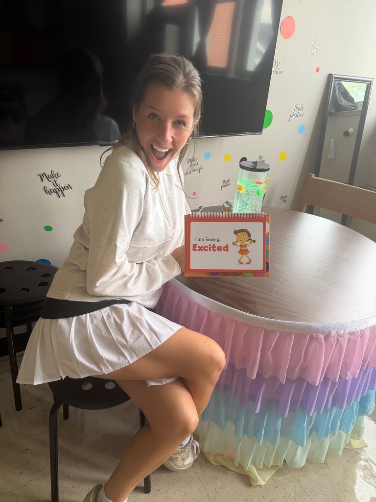A staff member setting up a school classroom, holding a "Excited," sign.