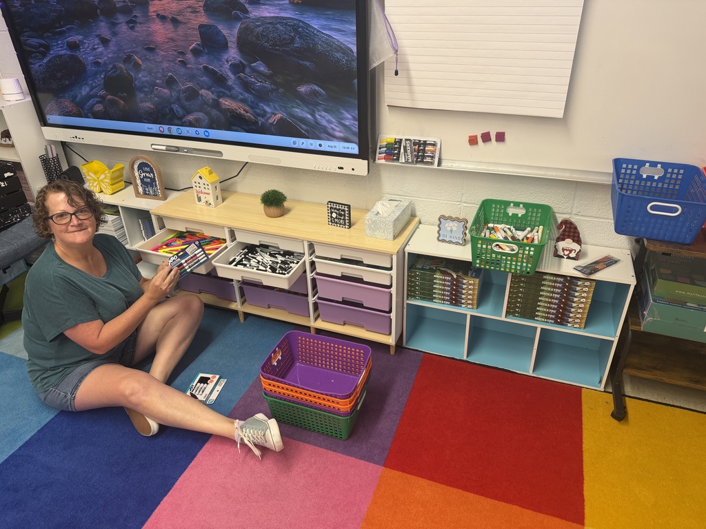 A staff member setting up a school classroom, holding up a pack of markers.