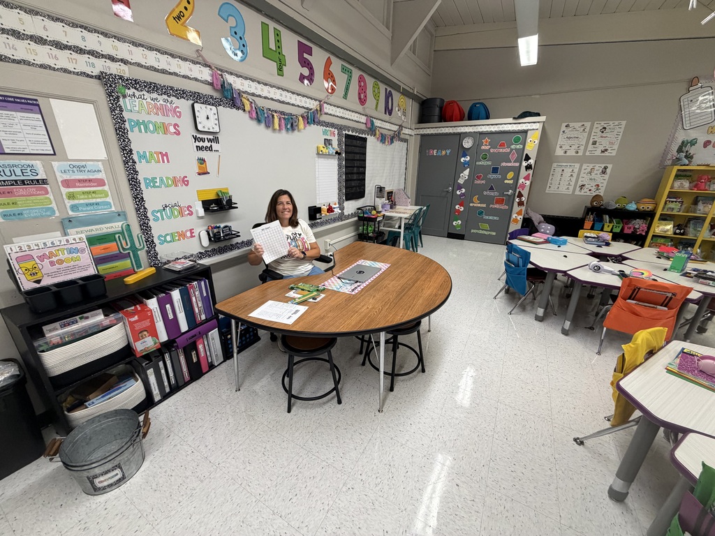 A staff member setting up a school classroom, holding up a notebook..