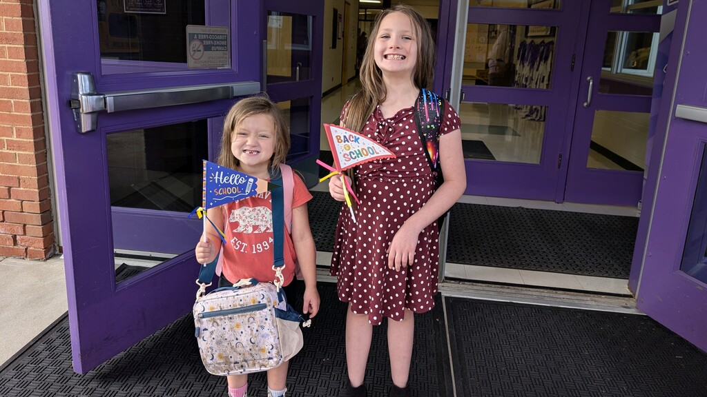 Two students holding back to school props while smiling.