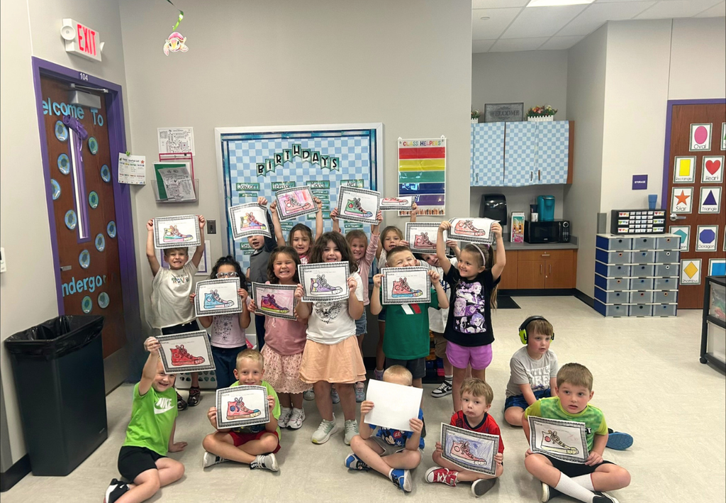 A group of young students holding up their artwork in a school classroom.