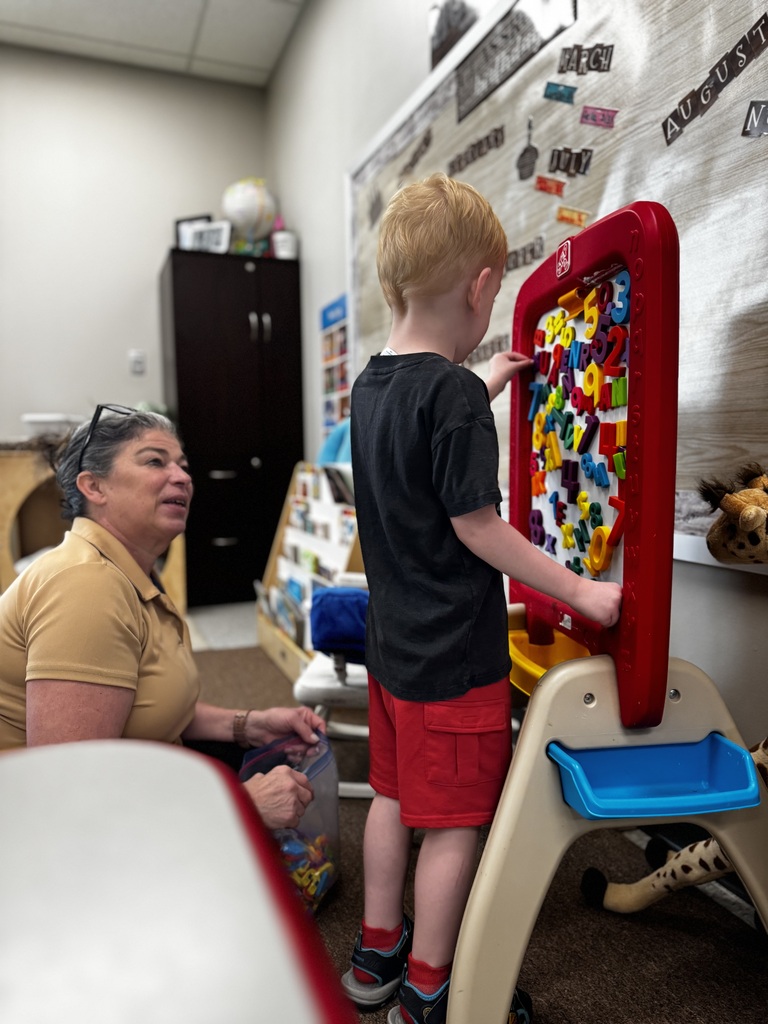 A young student using number and letter blocks in a school classroom with a staff member's help.
