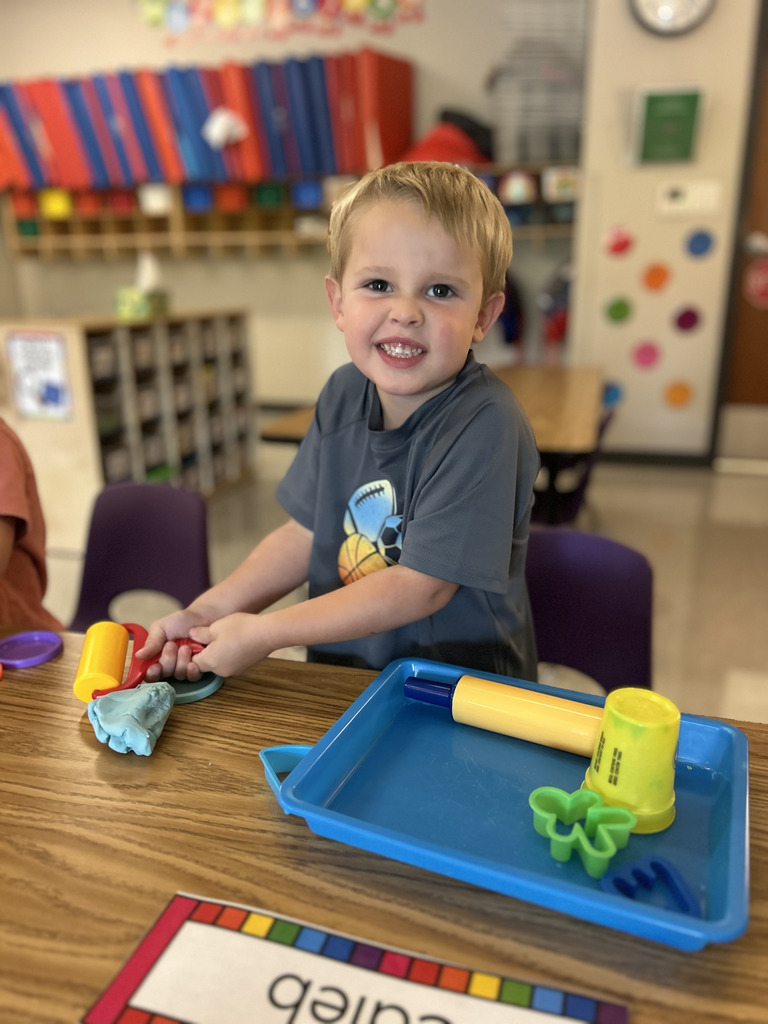 A young student playing with Play-dough in a school classroom.