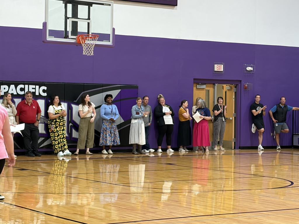 Staff members standing in a line in a purple school gym.