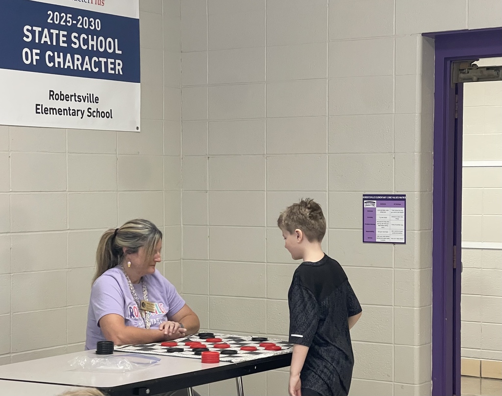 A staff member and a young student playing checkers.