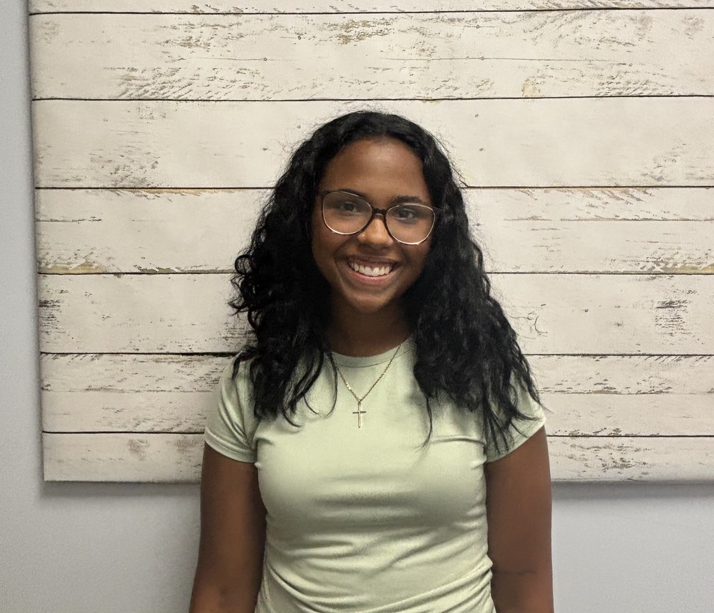 A student posing for a photo in front of a wooden wallpaper.
