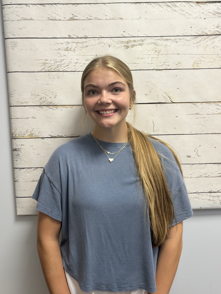 A student posing for a photo in front of a wooden wallpaper.