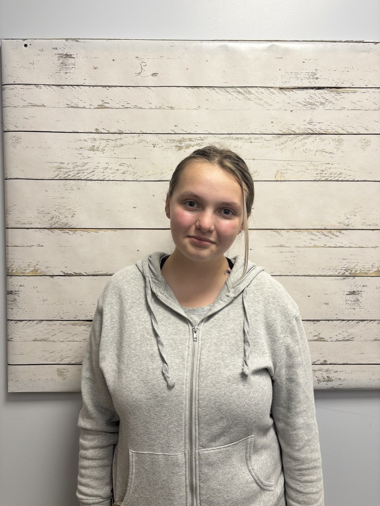 A student posing for a photo in front of a wooden wallpaper.